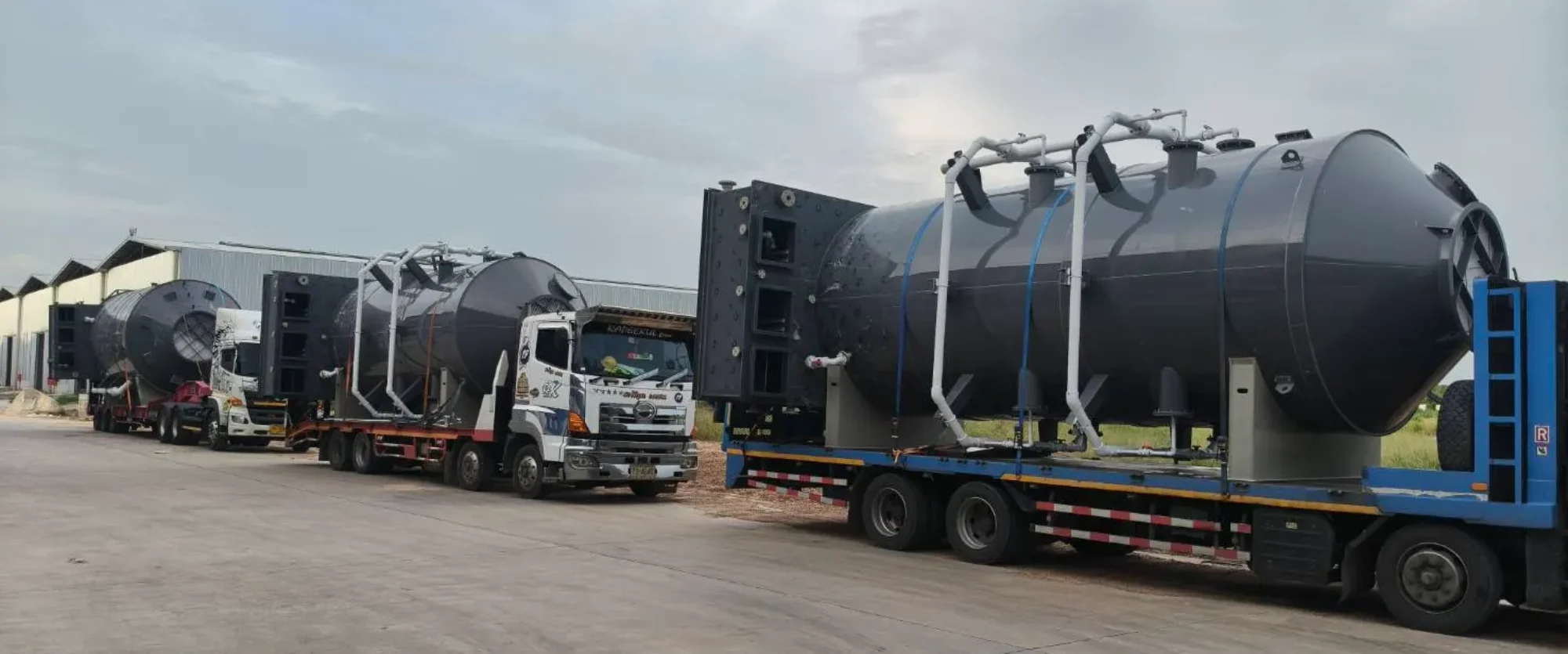 Large industrial tank cylinders loaded on flatbed trailers for transport at a loading yard.